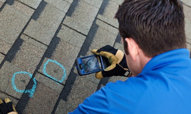 A person in gloves uses a smartphone to photograph two blue chalk circles on a roof.