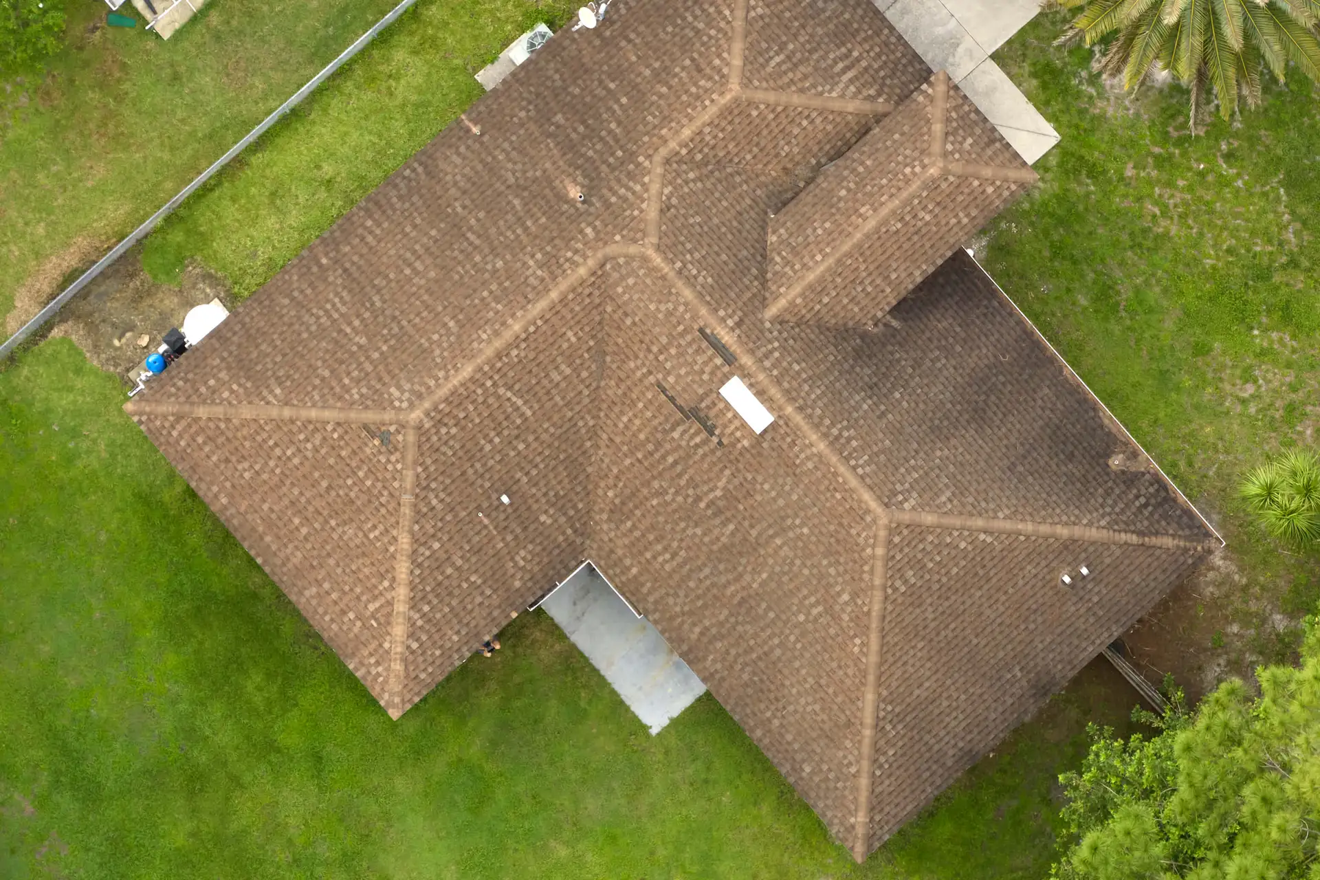 Top-down view of a brown-roofed house with a green lawn surrounding it.